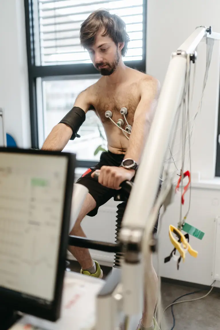 Sportovec šlape na bicyklovém ergometru s EKG svody, na monitoru běží záznam