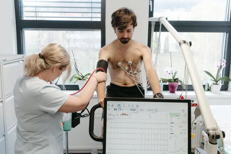 Sestra měří sportovci krevní tlak v průběhu zátěžového vyšetření, na monitoru běží EKG